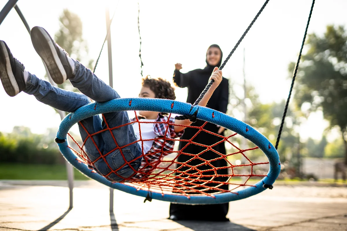 Mother in abaya pushing her son on a swing